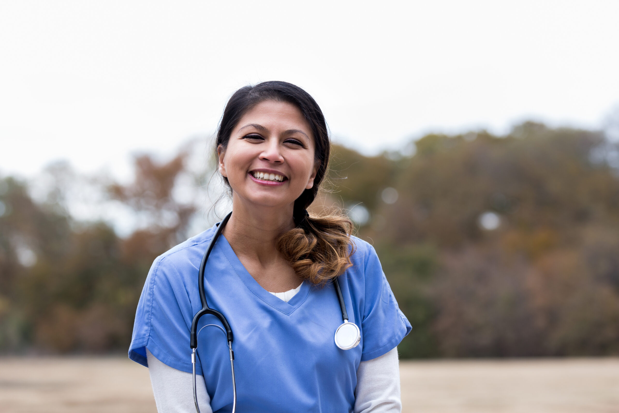 Confident mid adult female doctor or nurse smiles cheerfully at the camera while working at an outdoor free clinic.