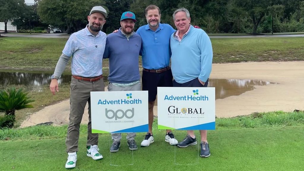 BPD team members at a charity golf outing holding AdventHealth Global sponsor signs